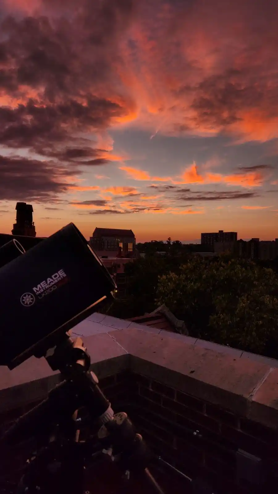 A photo of a telescope on the Nielsen Rooftop with a gorgeous sunset colored sky.