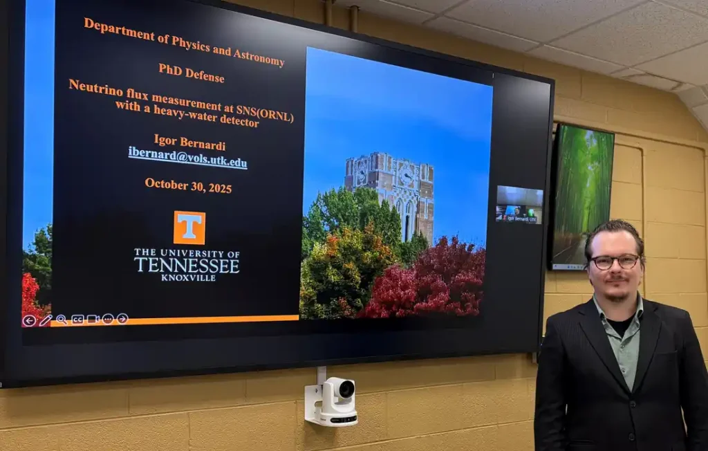 A man in front of a large screen presenting a doctoral dissertation defense
