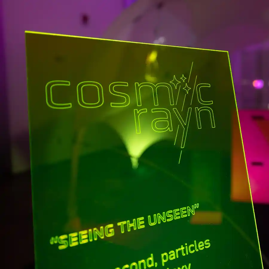 An etched translucent sign in green reading cosmicrayn, seeing the unseen