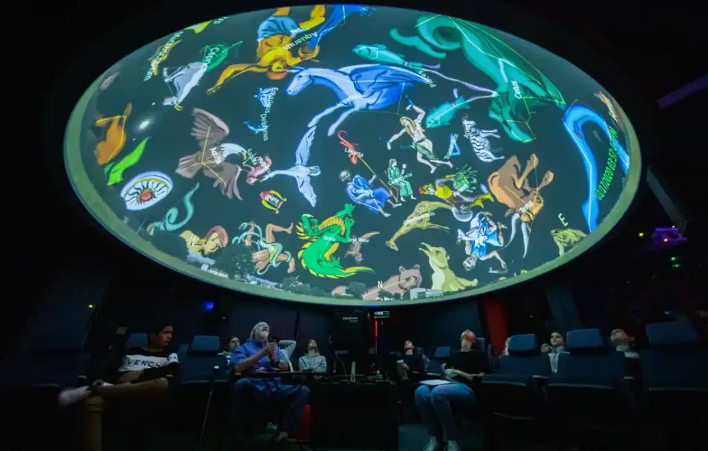 A group of people looking up at a colorful depiction of constellations on a planetarium dome