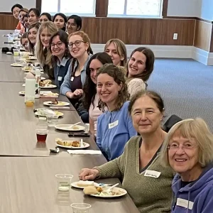 A photo of physics students, faculty, and postdocs at a long table.
